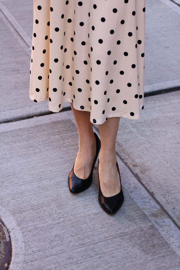 the lower half of a woman wearing a polka dot dress and dark heels
