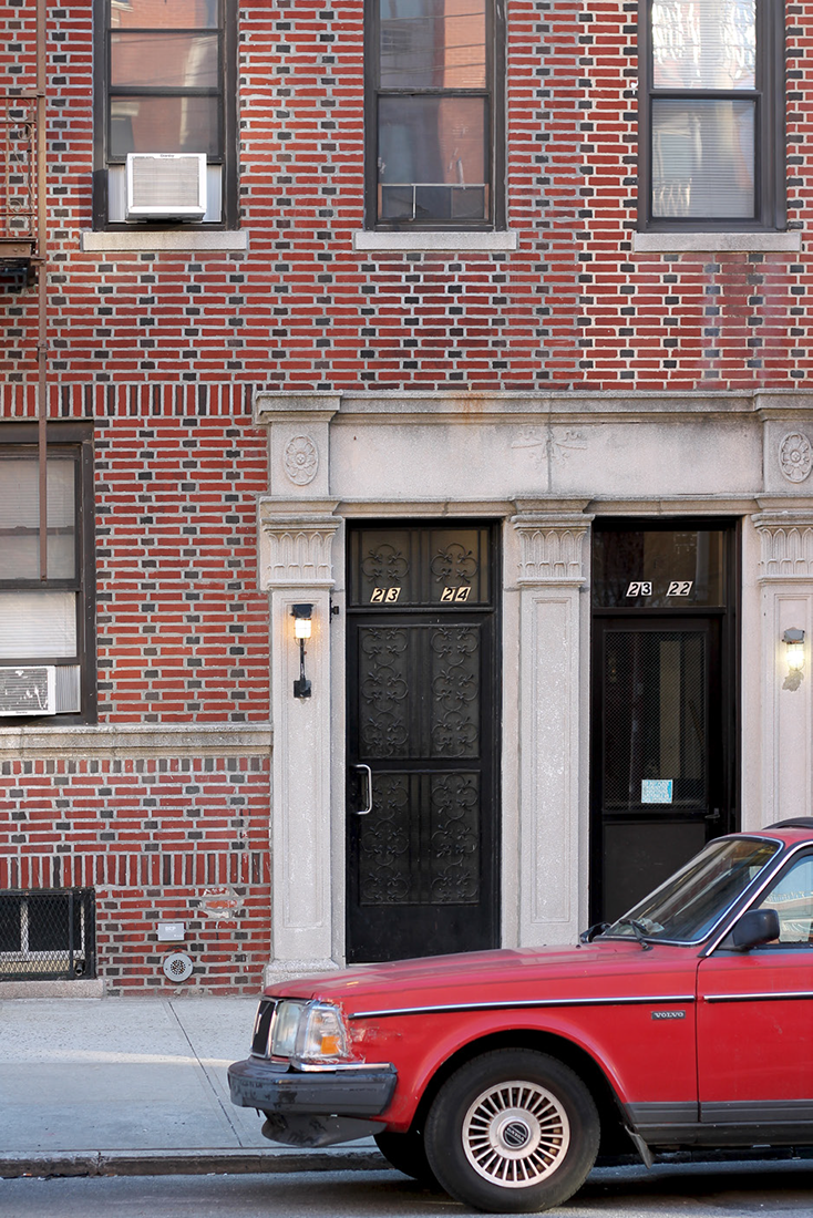 a red car parked in front of an apartment building numbered 23-24 and 23-22